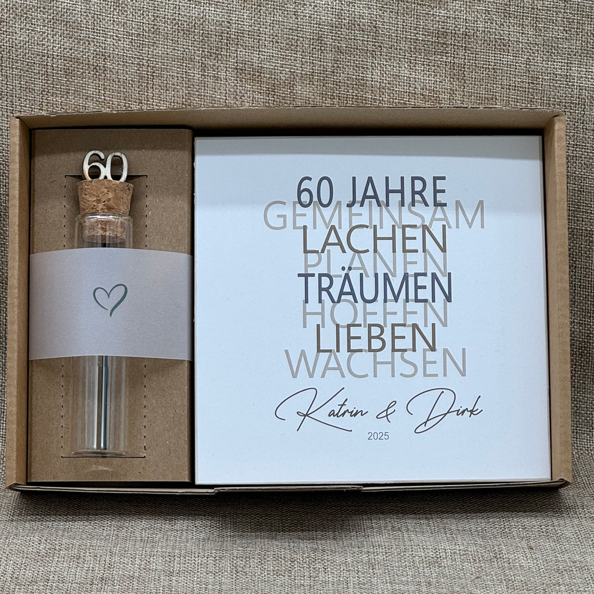 Dieses liebevolle Geschenkset zum 60. Hochzeitstag, der Diamantenen Hochzeit, besteht aus einem handgefertigten Holzblock mit inspirierenden Worten wie Lachen, Lieben und Wachsen. Auf Wunsch kann der Block mit Namen und Datum personalisiert werden. Dazu gibt es ein dekoratives Reagenzglas mit Holz-Zahl '60' für Geldgeschenke oder Gutscheine. Alles ist stilvoll verpackt in einer Geschenkbox mit Aufdruck „Der schönste Weg ist der Gemeinsame“.