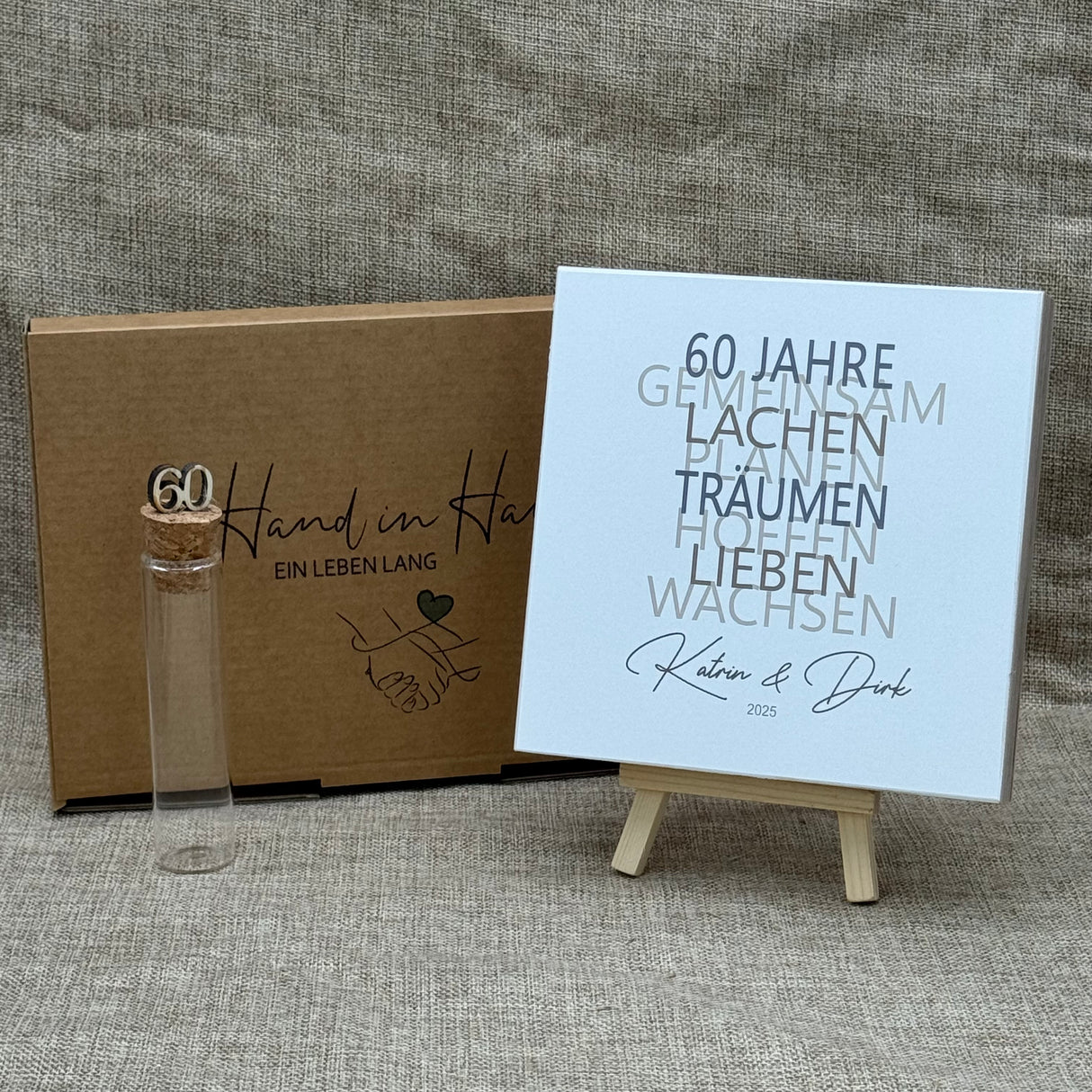 Zum 60. Hochzeitstag ist dieses Geschenkset eine wundervolle Erinnerung an gemeinsame Jahre. Es enthält einen handgefertigten Holzblock mit den Worten 60 Jahre, Lachen, Träumen, Lieben und Wachsen, personalisierbar mit Namen und Datum. Dazu ein Reagenzglas mit Holz-Zahl '60' für Geldgeschenke. Verpackt in einer liebevollen Geschenkbox mit dem Spruch „Der schönste Weg ist der Gemeinsame“ – perfekt für das Jubelpaar.