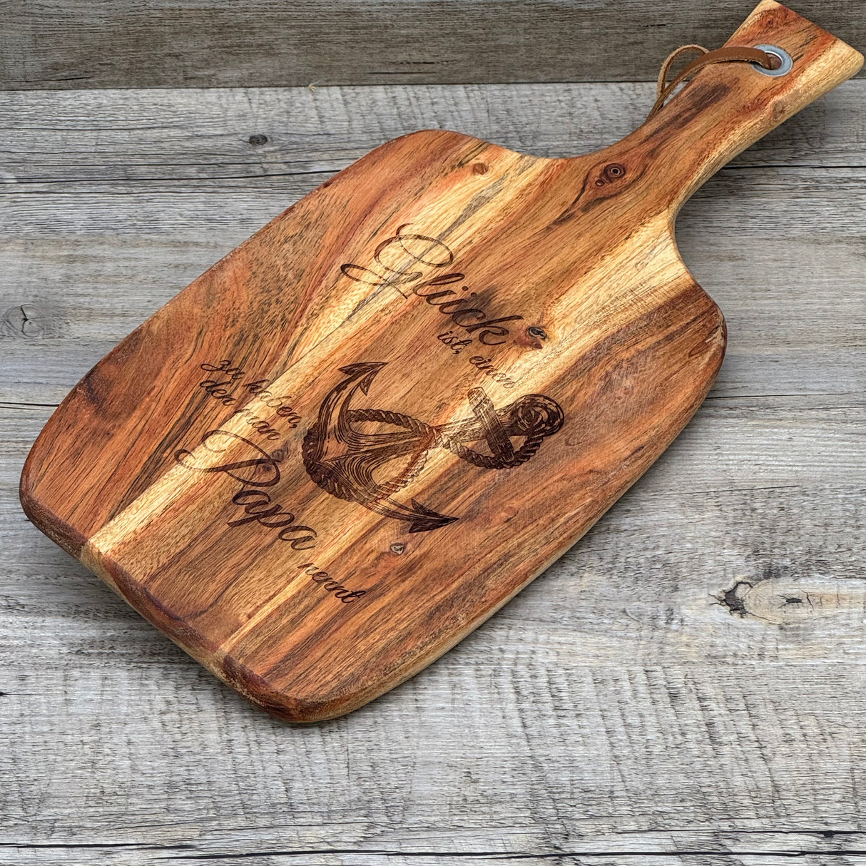 Dieses stilvolle Servierbrett eignet sich auch als Firmengeschenk oder besondere Aufmerksamkeit für Kunden oder Mitarbeiter, die Väter sind – zum Vatertag, Jubiläum oder als Dankeschön. Die Gravur „Glück ist ein Anker“ mit Anker-Motiv verleiht dem Brett Persönlichkeit und Bedeutung. Hergestellt aus langlebigem Akazienholz, vielseitig einsetzbar und dekorativ. Praktisches Lederband inklusive. Ein emotionales, hochwertiges Geschenk mit Stil.
