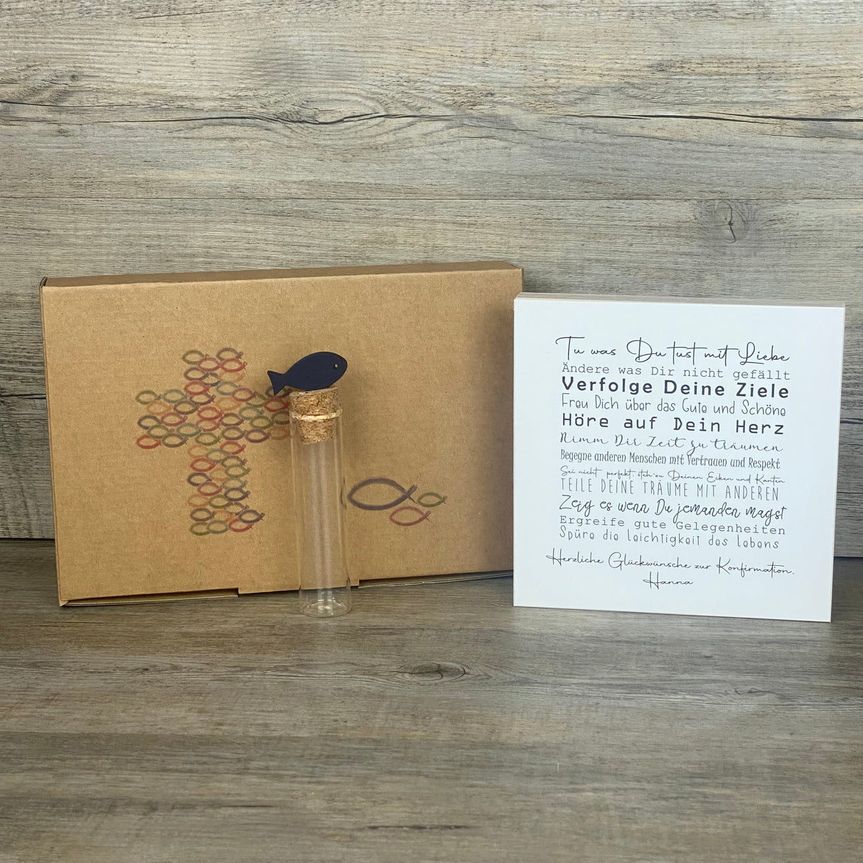 Feiere die Konfirmation mit einem besonderen Geschenkset: Ein personalisierbarer Wooden Block Art mit ermutigenden Sprüchen und ein Reagenzglas mit Fisch-Deko für Geldgeschenke oder Gutscheine. Der Block ist handgefertigt aus Naturmaterialien (15 x 15 x 2,2 cm) und wird zusammen mit der stilvollen Geschenkbox geliefert. Wähle zwischen Fisch- oder Kreuz-Motiv – ein persönliches, liebevoll hergestelltes Geschenk für Jungen und Mädchen.