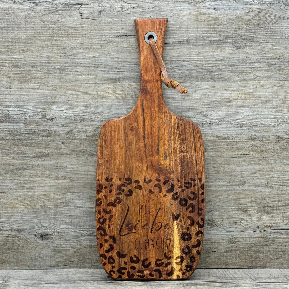 Dieses Servierbrett „Mit Liebe gemacht“ aus hochwertigem Akazienholz ist das perfekte Geschenk für deine Mama, Oma oder beste Freundin – ideal zum Geburtstag, Einzug oder einfach als liebevolle Aufmerksamkeit. Die feine Lasergravur verleiht ihm eine persönliche Note, das Lederband ermöglicht praktisches Aufhängen. Vielseitig nutzbar als Schneide- oder Servierbrett oder als dekoratives Highlight. Natürlich, langlebig und stilvoll. Ein Geschenk, das Herz und Küche verbindet.