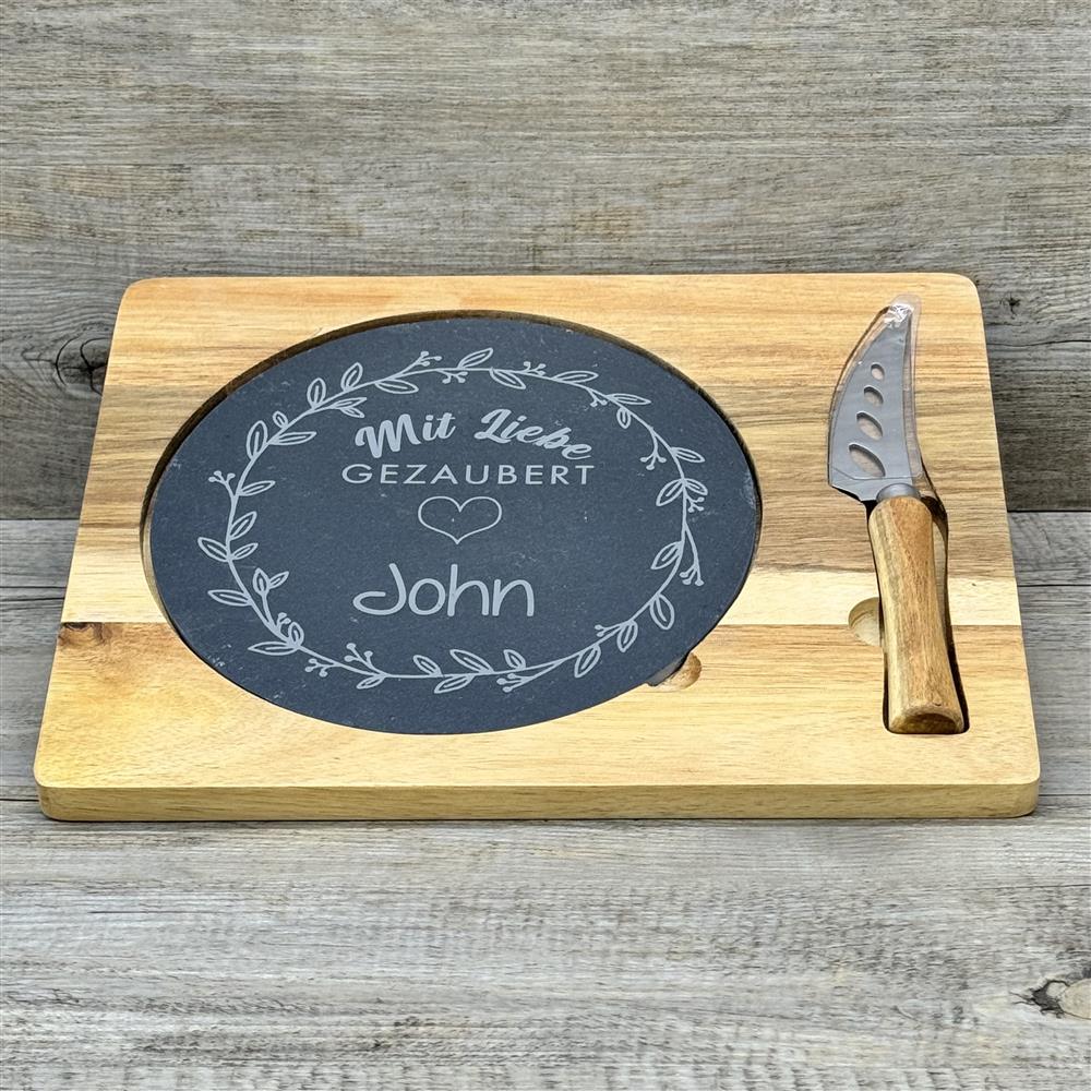 Diese personalisierte Schiefer-Servierplatte „Mit Liebe gezaubert“ ist ein besonderes Geschenk für Familie oder Freunde. Mit zusätzlichem Wunschnamen wird sie zu einem einzigartigen Highlight für Küche und Tisch. Ideal zum stilvollen Anrichten von Käse, Antipasti oder Snacks. Hochwertiges Akazienholzbrett, Naturschieferplatte und Edelstahlmesser mit Holzgriff verbinden Design und Funktion. Ein dekoratives, praktisches und persönliches Präsent für Genießer.