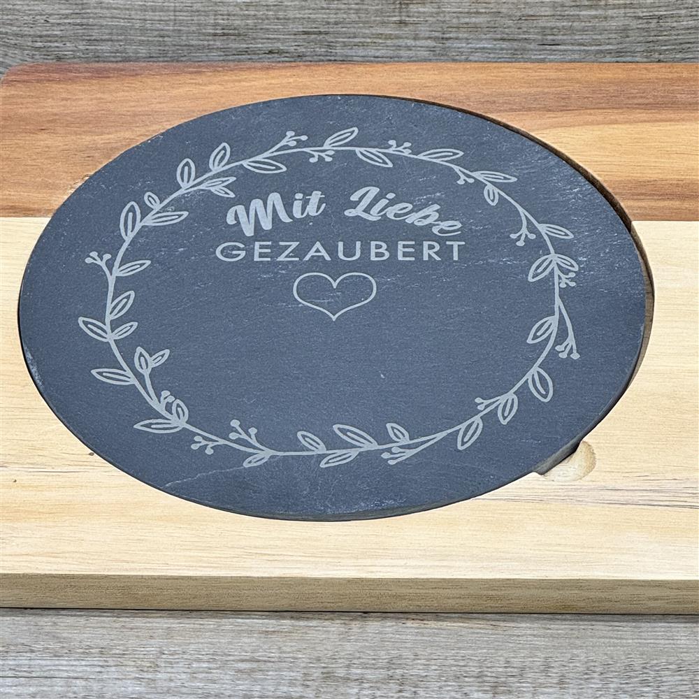 Diese personalisierte Schiefer-Servierplatte „Mit Liebe gezaubert“ ist ein besonderes Geschenk für Familie oder Freunde. Mit zusätzlichem Wunschnamen wird sie zu einem einzigartigen Highlight für Küche und Tisch. Ideal zum stilvollen Anrichten von Käse, Antipasti oder Snacks. Hochwertiges Akazienholzbrett, Naturschieferplatte und Edelstahlmesser mit Holzgriff verbinden Design und Funktion. Ein dekoratives, praktisches und persönliches Präsent für Genießer.