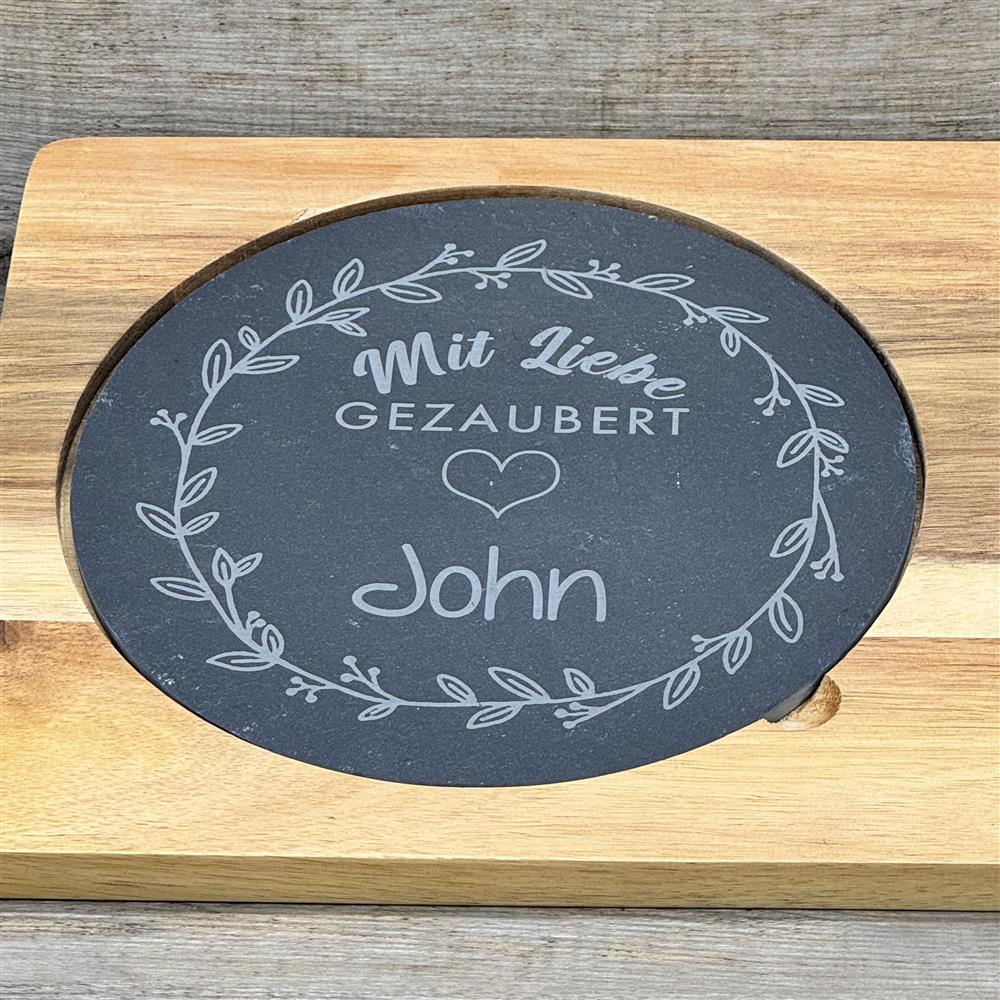 Ein liebevolles Geschenk für Freunde, Paare oder Familie: die Schiefer-Servierplatte „Mit Liebe gezaubert“ mit personalisierbarem Namen. Perfekt für Geburtstage, Einweihungen oder Weihnachten, zum stilvollen Servieren von Käse, Tapas oder kleinen Snacks. Naturschiefer, Akazienholzbrett und Edelstahlmesser sorgen für Qualität und Eleganz. Ein dekoratives, praktisches und individuelles Küchenaccessoire voller Charme.