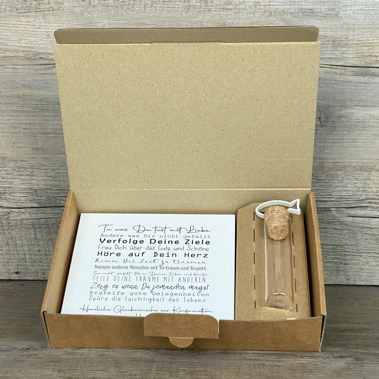 Feiere die Konfirmation mit einem besonderen Geschenkset: Ein personalisierbarer Wooden Block Art mit ermutigenden Sprüchen und ein Reagenzglas mit Fisch-Deko für Geldgeschenke oder Gutscheine. Der Block ist handgefertigt aus Naturmaterialien (15 x 15 x 2,2 cm) und wird zusammen mit der stilvollen Geschenkbox geliefert. Wähle zwischen Fisch- oder Kreuz-Motiv – ein persönliches, liebevoll hergestelltes Geschenk für Jungen und Mädchen.