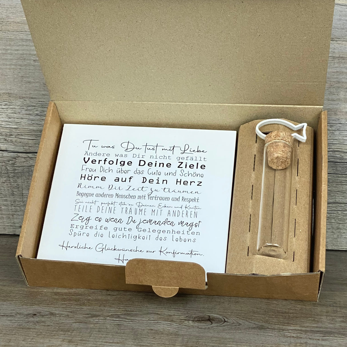 Feiere die Konfirmation mit einem besonderen Geschenkset: Ein personalisierbarer Wooden Block Art mit ermutigenden Sprüchen und ein Reagenzglas mit Fisch-Deko für Geldgeschenke oder Gutscheine. Der Block ist handgefertigt aus Naturmaterialien (15 x 15 x 2,2 cm) und wird zusammen mit der stilvollen Geschenkbox geliefert. Wähle zwischen Fisch- oder Kreuz-Motiv – ein persönliches, liebevoll hergestelltes Geschenk für Jungen und Mädchen.