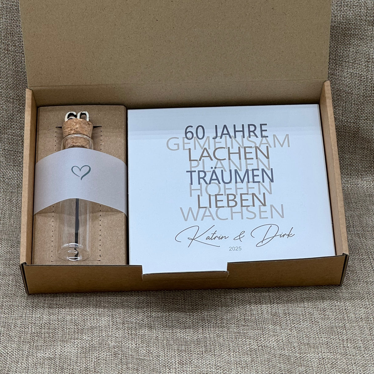 Zum 60. Hochzeitstag ist dieses Geschenkset eine wundervolle Erinnerung an gemeinsame Jahre. Es enthält einen handgefertigten Holzblock mit den Worten 60 Jahre, Lachen, Träumen, Lieben und Wachsen, personalisierbar mit Namen und Datum. Dazu ein Reagenzglas mit Holz-Zahl '60' für Geldgeschenke. Verpackt in einer liebevollen Geschenkbox mit dem Spruch „Der schönste Weg ist der Gemeinsame“ – perfekt für das Jubelpaar.
