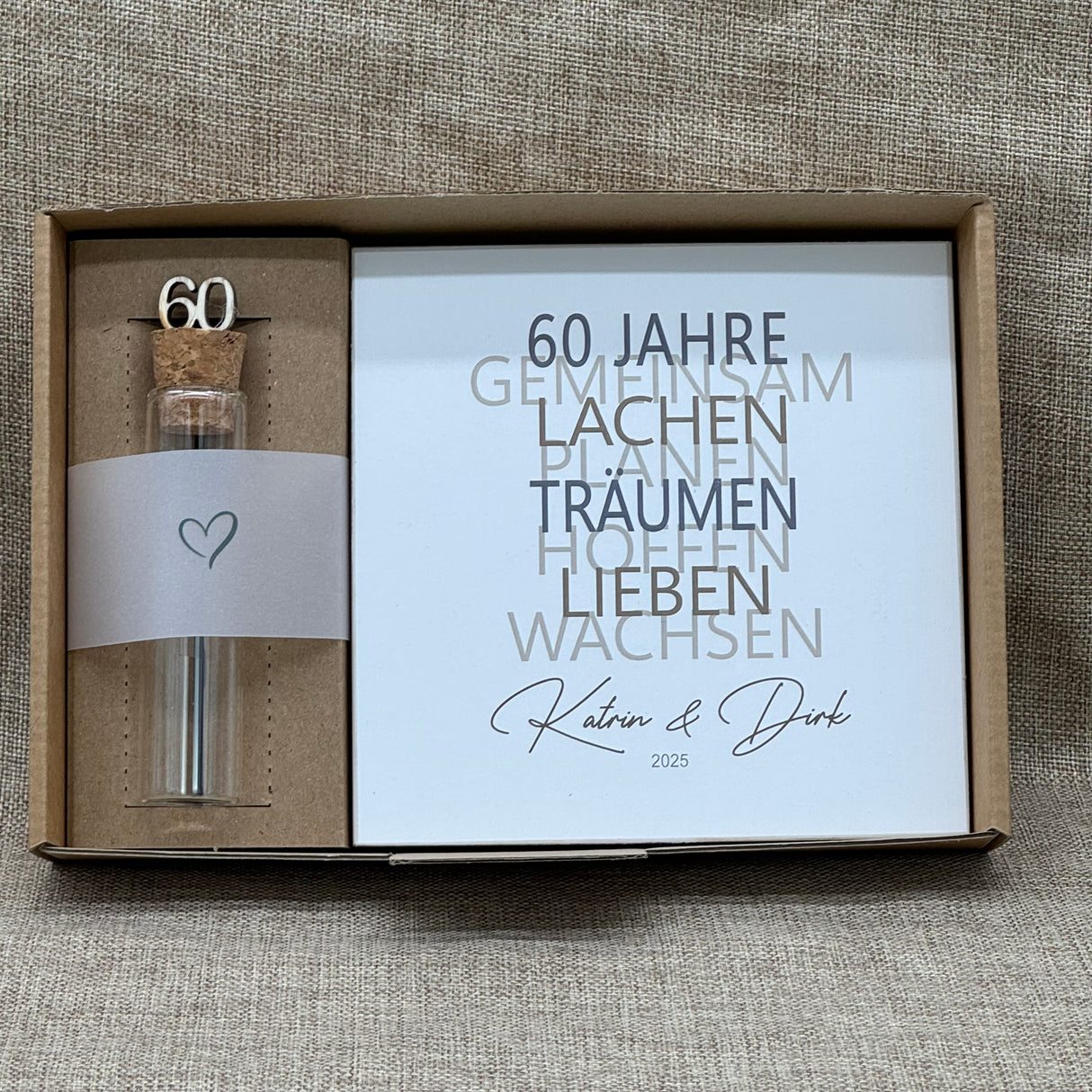 Feiere die Diamantene Hochzeit mit diesem stilvollen Geschenkset. Ein personalisierbarer Holzblock mit Aufschrift wie Lieben, Hoffen, Wachsen erinnert an 60 gemeinsame Jahre. Ein dekoratives Reagenzglas mit Holz-Zahl '60' eignet sich ideal für Gutscheine oder Geldgeschenke. Das Set wird in einer hochwertigen Geschenkbox mit dem Spruch „Der schönste Weg ist der Gemeinsame“ geliefert und ist ein einzigartiges Präsent für das Jubelpaar.
