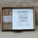 Feiere die Diamantene Hochzeit mit diesem stilvollen Geschenkset. Ein personalisierbarer Holzblock mit Aufschrift wie Lieben, Hoffen, Wachsen erinnert an 60 gemeinsame Jahre. Ein dekoratives Reagenzglas mit Holz-Zahl '60' eignet sich ideal für Gutscheine oder Geldgeschenke. Das Set wird in einer hochwertigen Geschenkbox mit dem Spruch „Der schönste Weg ist der Gemeinsame“ geliefert und ist ein einzigartiges Präsent für das Jubelpaar.
