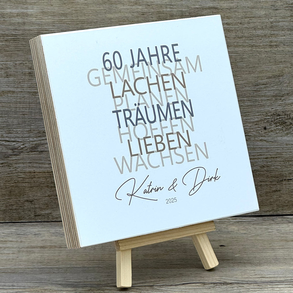 Dieses liebevolle Geschenkset zum 60. Hochzeitstag, der Diamantenen Hochzeit, besteht aus einem handgefertigten Holzblock mit inspirierenden Worten wie Lachen, Lieben und Wachsen. Auf Wunsch kann der Block mit Namen und Datum personalisiert werden. Dazu gibt es ein dekoratives Reagenzglas mit Holz-Zahl '60' für Geldgeschenke oder Gutscheine. Alles ist stilvoll verpackt in einer Geschenkbox mit Aufdruck „Der schönste Weg ist der Gemeinsame“.
