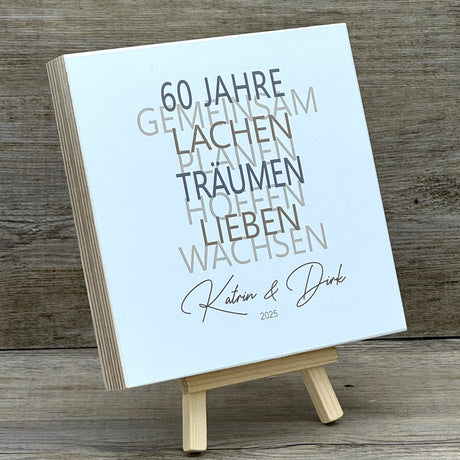 Dieses liebevolle Geschenkset zum 60. Hochzeitstag, der Diamantenen Hochzeit, besteht aus einem handgefertigten Holzblock mit inspirierenden Worten wie Lachen, Lieben und Wachsen. Auf Wunsch kann der Block mit Namen und Datum personalisiert werden. Dazu gibt es ein dekoratives Reagenzglas mit Holz-Zahl '60' für Geldgeschenke oder Gutscheine. Alles ist stilvoll verpackt in einer Geschenkbox mit Aufdruck „Der schönste Weg ist der Gemeinsame“.
