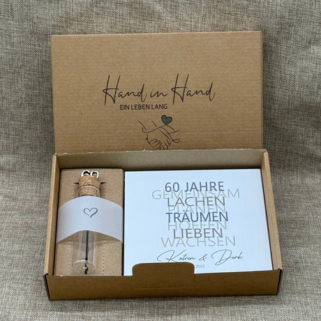 Dieses liebevolle Geschenkset zum 60. Hochzeitstag, der Diamantenen Hochzeit, besteht aus einem handgefertigten Holzblock mit inspirierenden Worten wie Lachen, Lieben und Wachsen. Auf Wunsch kann der Block mit Namen und Datum personalisiert werden. Dazu gibt es ein dekoratives Reagenzglas mit Holz-Zahl '60' für Geldgeschenke oder Gutscheine. Alles ist stilvoll verpackt in einer Geschenkbox mit Aufdruck „Der schönste Weg ist der Gemeinsame“.
