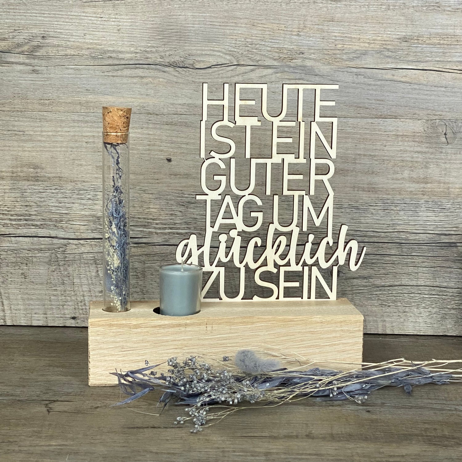 Verschenke Freude mit dem Deko Aufsteller Deluxe „Heute ist ein guter Tag um glücklich zu sein“.  
Gefertigt aus hochwertigem Eichenholz, Schriftzug aus Pappelholz, inklusive Reagenzglas mit Trockenblumen und Kerze.  
Größe Aufsteller: ca. 20 x 6 x 5 cm, Schriftzug ca. 15 x 18 cm, Geschenkverpackung ca. 25 x 20 x 7 cm.  
Trockenblumen und Kerze in Blau oder Rot erhältlich – Naturprodukt, Abweichungen möglich.  
Personalisierbar mit Namen, Datum oder Koordinaten – ein individuelles Geschenk für jeden Anlass.