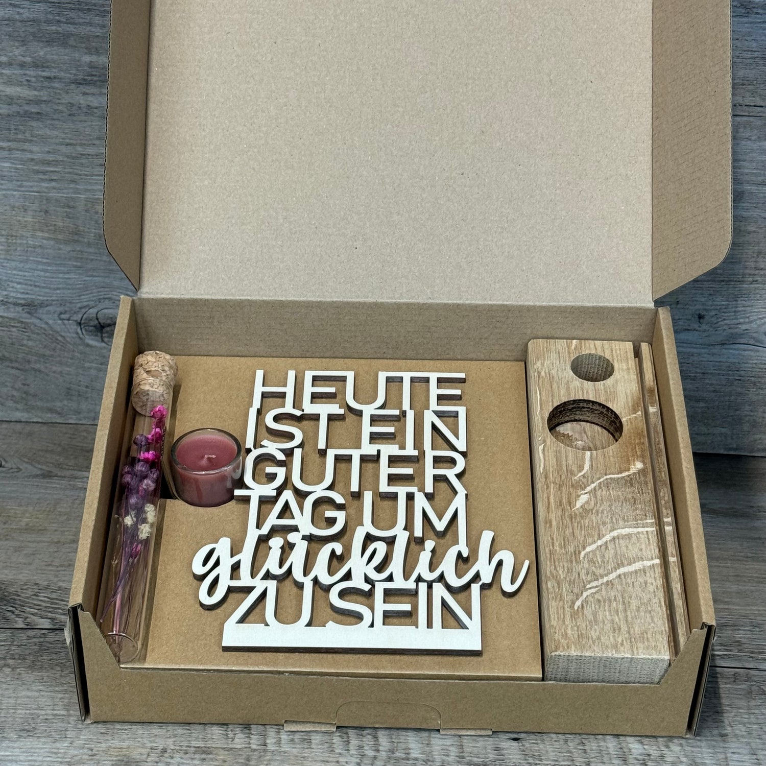 Der Deko Aufsteller Deluxe „Heute ist ein guter Tag um glücklich zu sein“ ist ein wunderschöner Blickfang für jede Wohnung.  
Aus Eichenholz gefertigt, Schriftzug aus 3 mm Pappelholz, mit Reagenzglas voller Trockenblumen und Kerze.  
Maße: ca. 20 x 6 x 5 cm, Geschenkverpackung ca. 25 x 20 x 7 cm, Trockenblumen und Kerze wählbar in Blau oder Rot.  
Personalisierbar mit Namen, Daten oder Koordinaten für ein einzigartiges, persönliches Geschenk.  
Perfekt als Geburtstags-, Hochzeits- oder Verlobungsgeschenk fü